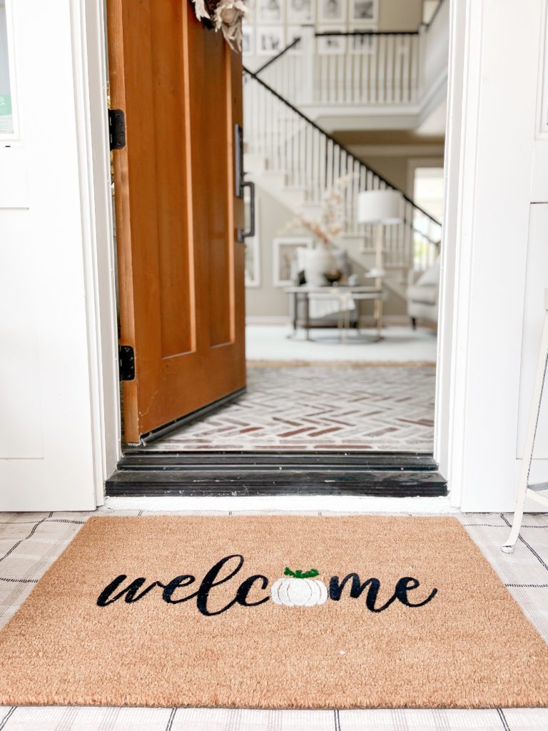 A fall welcome door mat on a front porch with the door open