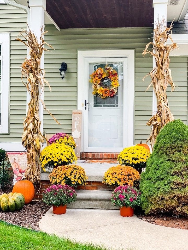 Fall front porch decor with corn stalks, mums, and pumpkins on a brick stoop