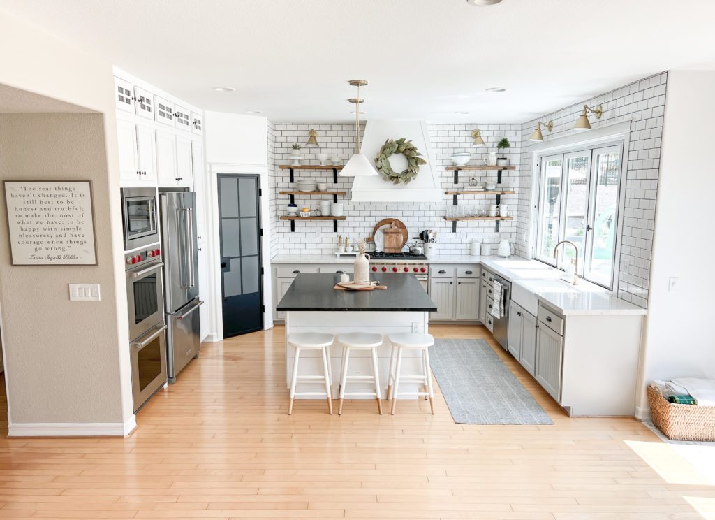 Kitchen remodel inspiration full kitchen view Sherwin williams pure white cabinets and a black metal pantry door and bifold window with open shelves and gold sconces