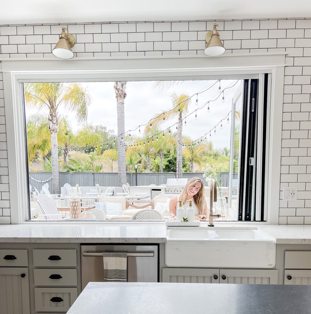 Kitchen remodel with white subway tile and white lyra quartz countertops and soapstone countertops with gold lighting and gold faucet and black metal pantry door and open shelves.  Panoramic bifold window and Panoramic bifold doors