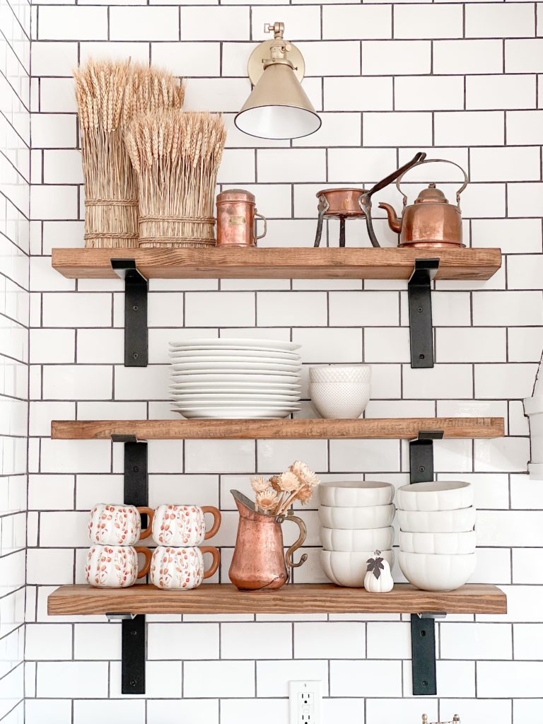 Easy ways to add fall decor to the kitchen | Fall decor inspiration | Fall decor in the kitchen | Kitchen decorating ideas for fall | Fall decor on open shelves in a kitchen | Faux pumpkins and vintage copper for fall decor | Gold faucet and glass soap bottles for fall decorations | Fall dish towels 